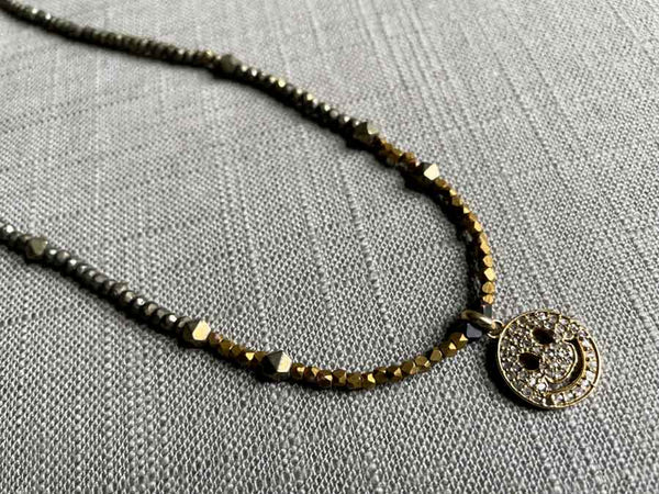 closeup of pave smiley face pendant hung on a metallic bead choker