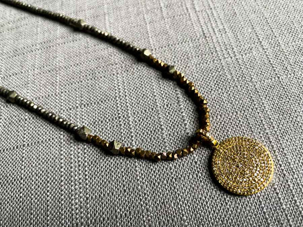 closeup of pave disc pendant hung on a metallic bead choker