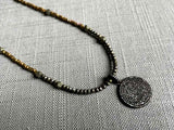 closeup of pave disc pendant hung on a metallic bead choker