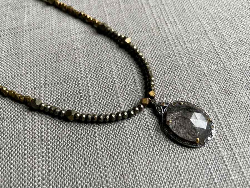 closeup of pave tourmalated quartz pendant hung on a metallic bead choker