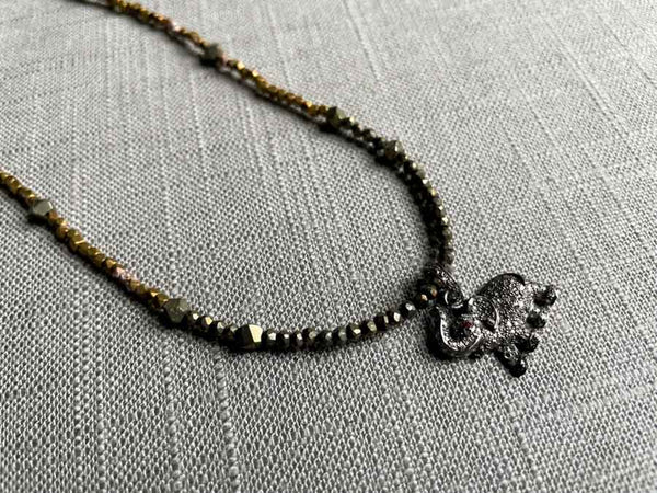 closeup of pave elephant pendant with ruby eye hung on a metallic bead choker