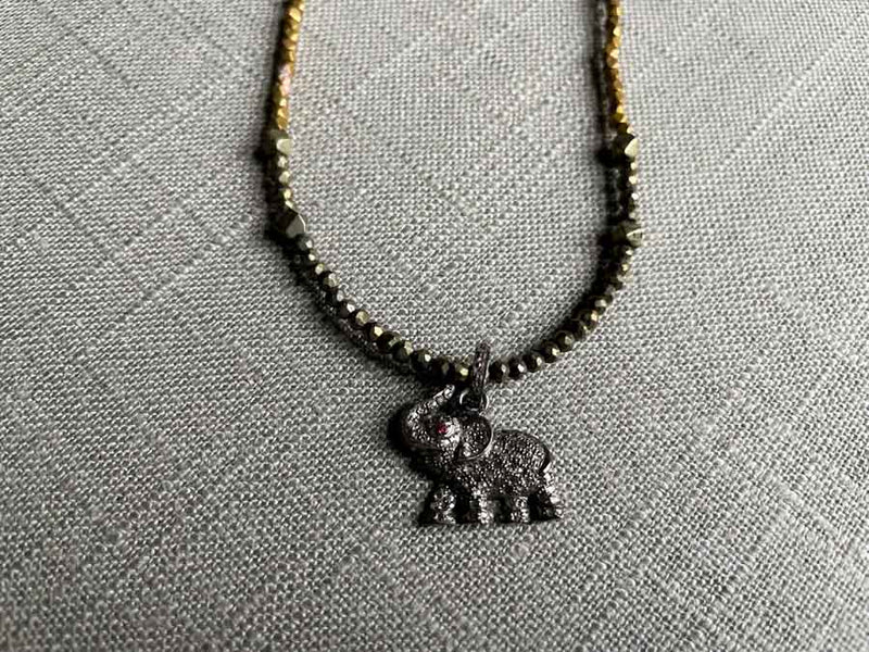 closeup of pave elephant pendant with ruby eye hung on a metallic bead choker