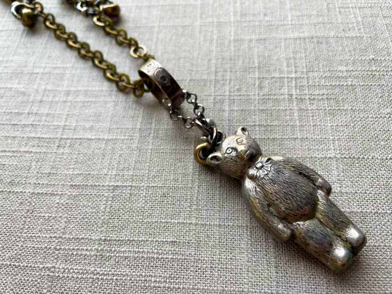 closeup of antique sterling silver bear rattle pendant on chain mix