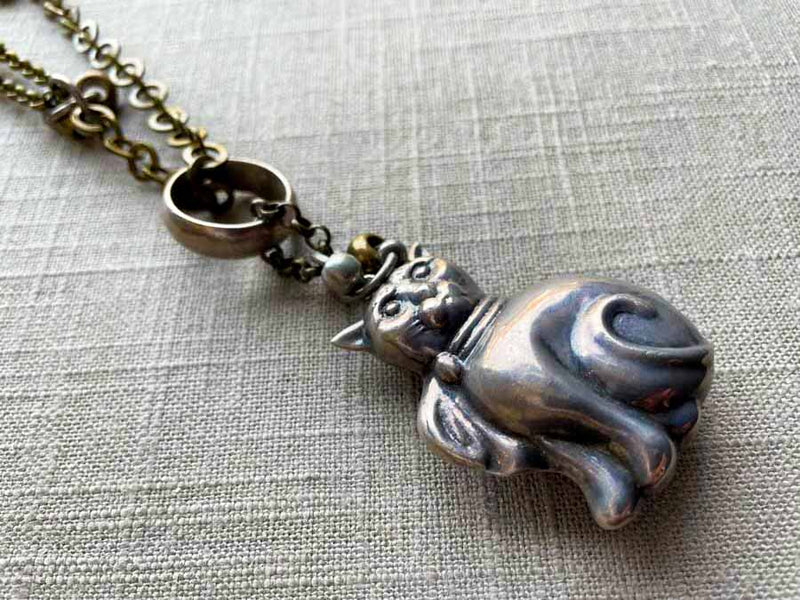 closeup of antique sterling silver cat rattle pendant on chain mix