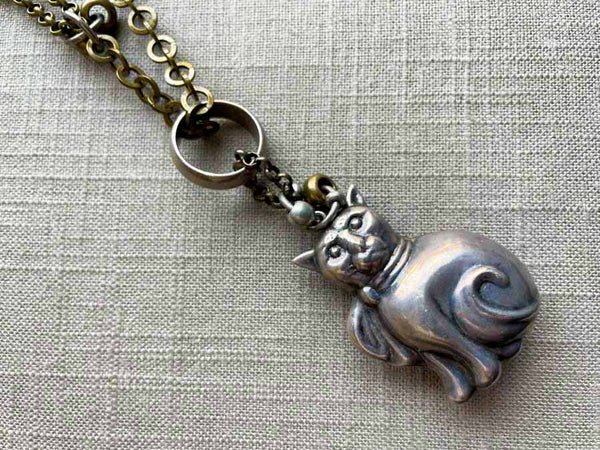 closeup of antique sterling silver cat rattle pendant on chain mix