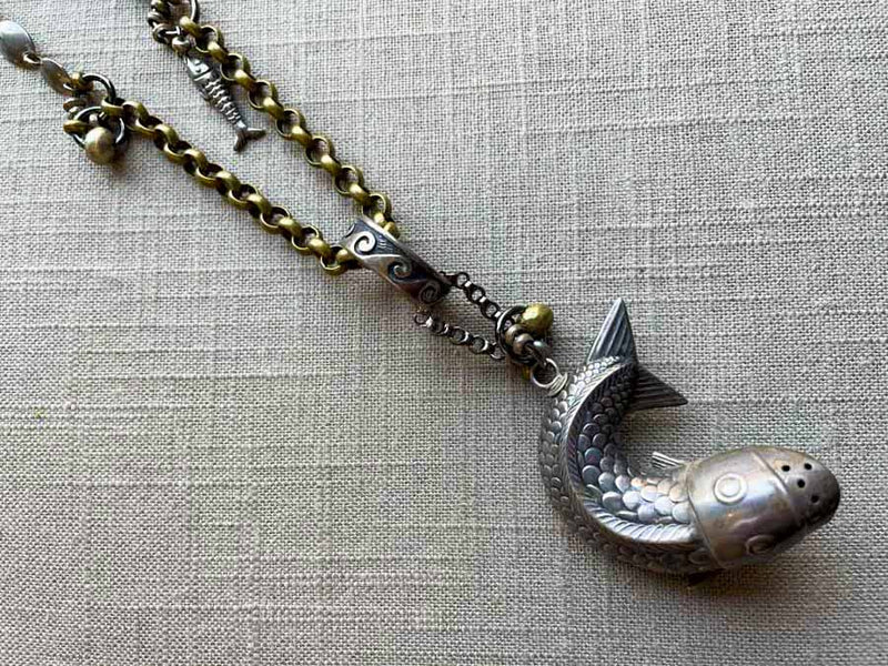 closeup of antique sterling silver fish salt shaker pendant on chain mix