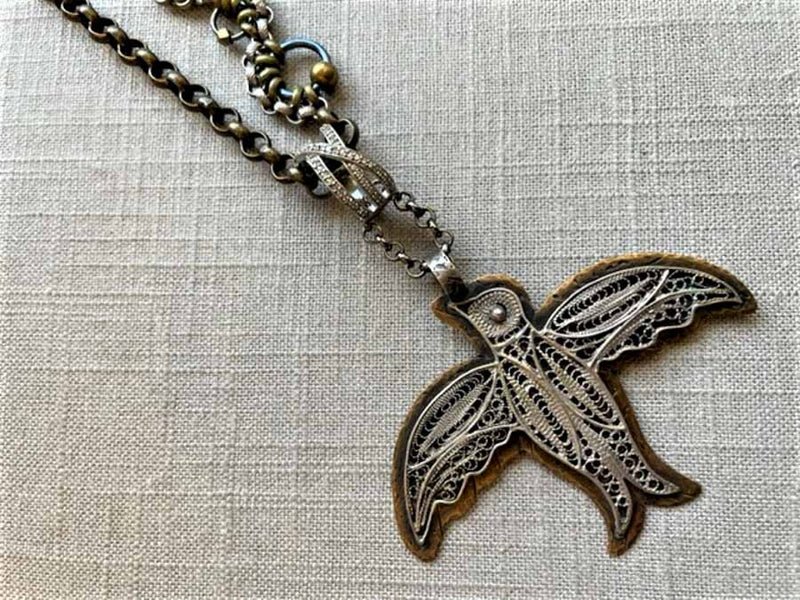 closeup of antique filigree bird pendant on chain mix