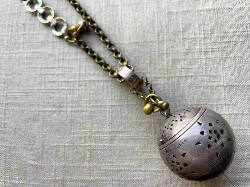 closeup of antique sterling silver globe tea caddy on chain mix