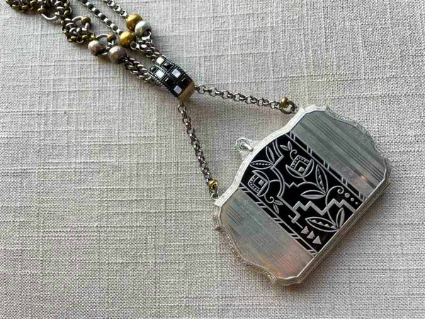 closeup of antique sterling silver compact pendant with black enamel on chain mix