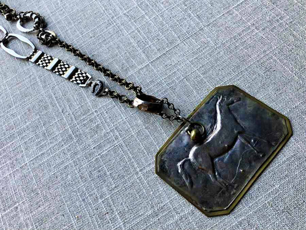 closeup of antique standing horse pendant on chain mix