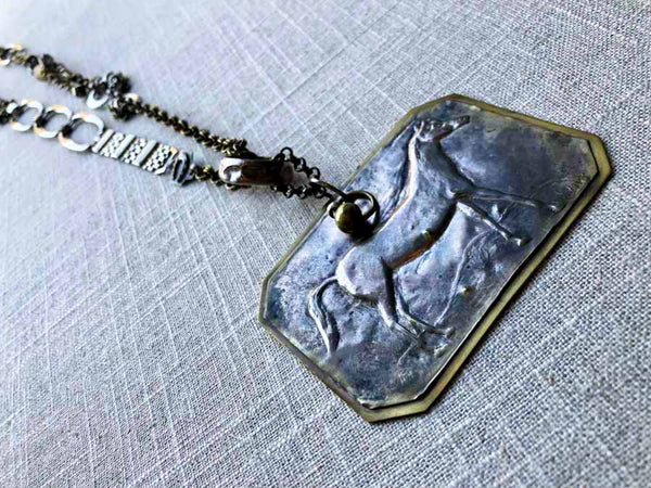 closeup of antique standing horse pendant on chain mix